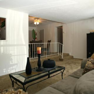 A cozy living room with a glass coffee table, decorative vases, and a view into the dining area.