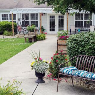A charming garden patio with a pathway, featuring a bench and vibrant plants in pots.