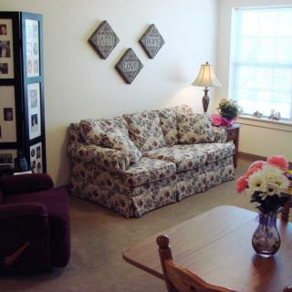 A cozy living room with a floral sofa, lamp, and decorated walls.
