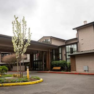 The main entrance of a modern building with a canopy and landscaped surroundings on a cloudy day.