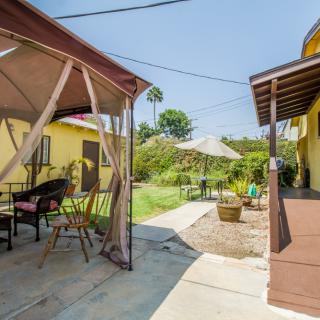A cozy backyard featuring a patio with a gazebo and outdoor seating, surrounded by lush greenery on a sunny day.
