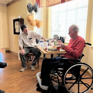 A caregiver engages with an elderly person in a wheelchair during a moment of connection.