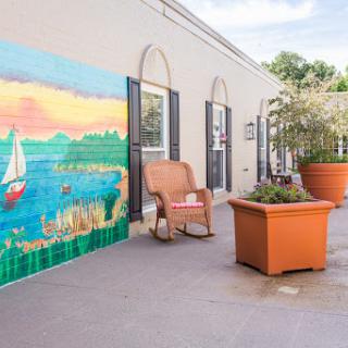 A serene outdoor space featuring a vibrant mural of a lake with sailboats, accompanied by comfortable seating and potted plants.