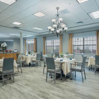 A modern dining room with neatly arranged tables and chairs, illuminated by a central chandelier.
