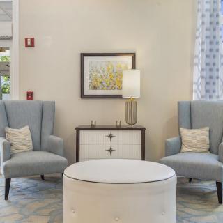 A cozy living room seating area featuring two armchairs and an ottoman, plemented by a lamp and artwork on the wall.