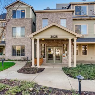 Entrance of a modern residential apartment building with brick exterior and landscaped walkway.