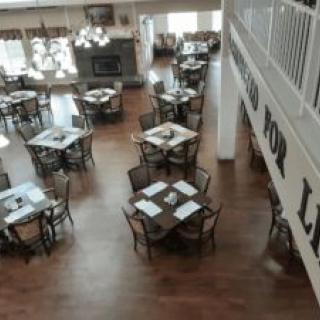 An empty restaurant dining area with neatly arranged tables and chairs on a wooden floor.