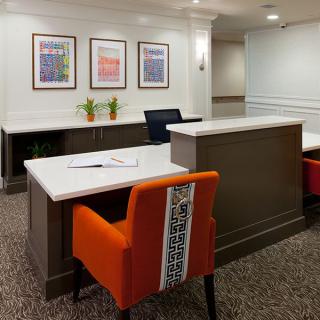 A modern reception area featuring a desk, vibrant orange chairs, and framed artwork on the wall.