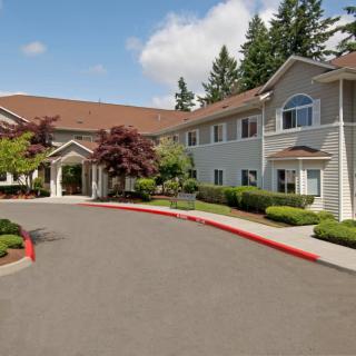 A spacious residential building with neatly landscaped surroundings and a driveway, set under a partly cloudy sky.
