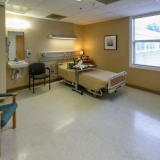 A hospital room with a single bed, chairs, and medical equipment.