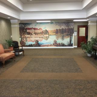 A spacious lobby featuring a serene mural, comfortable seating, and lush greenery.