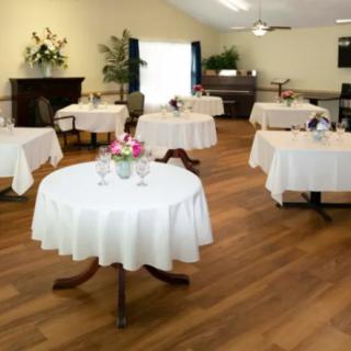 An elegantly set dining room with round tables covered in white tablecloths and decorated with flowers.