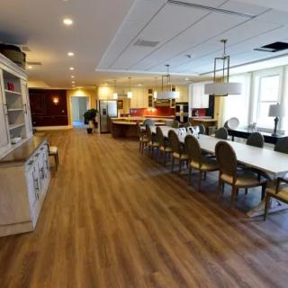A spacious dining area featuring a long table with chairs, modern lighting fixtures, and a wooden floor.