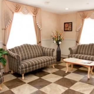A cozy living room featuring striped sofas, a coffee table, and checkered flooring, adorned with curtains and decorative plants.