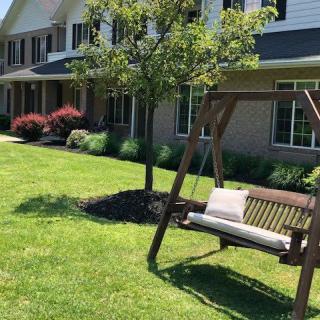 A peaceful garden scene with a wooden swing in front of a house.