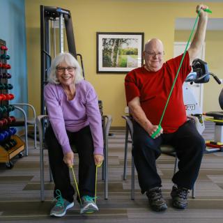 Two seniors exercising with resistance bands in a fitness room.