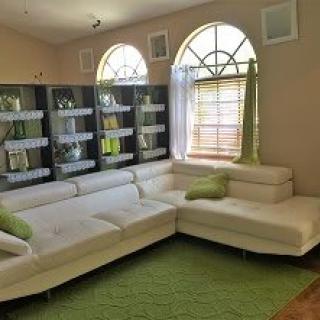 A modern living room featuring a white sectional sofa with green decorative pillows, a green rug, and arched windows.
