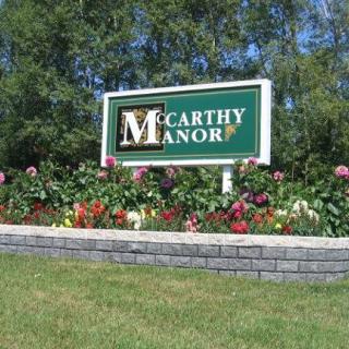 A sign for McCarthy Manor surrounded by colorful flowers and lush greenery.