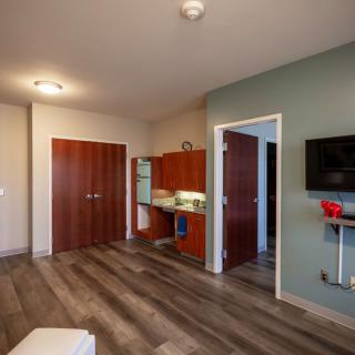 A modern apartment interior featuring a small kitchen, wood flooring, and minimalist furniture.
