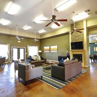 A spacious and modern living room featuring comfortable seating, a fireplace, and ceiling fans under bright lighting.