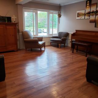 A cozy living room featuring wooden floors, a piano, and comfortable seating by the window.