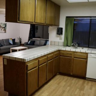 A cozy kitchen with wooden cabinets and a tiled countertop, adjacent to a living room.