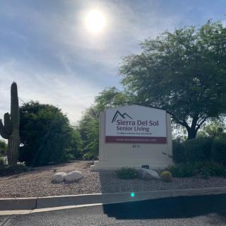 Sunlit landscape with a sign and surrounding trees and cactus.