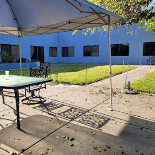 A peaceful outdoor courtyard featuring a table under a tent, surrounded by lush grass and a building.