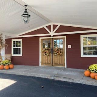 An entrance decorated with pumpkins and fall wreaths, featuring a wooden door on a red building.