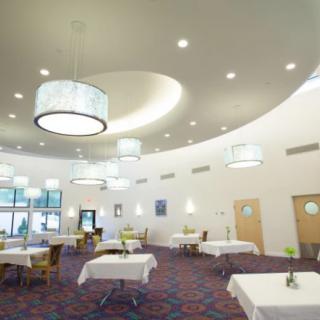 A spacious and modern dining area with white tablecloths, stylish lighting fixtures, and a patterned carpet.