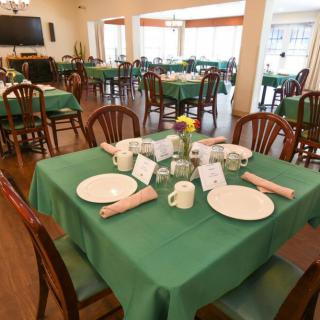 A well-arranged dining area with tables set for guests, featuring green tablecloths and wooden chairs.