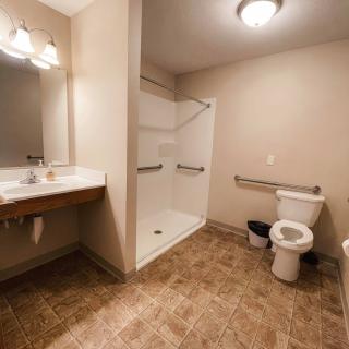 An accessible bathroom featuring a roll-in shower, toilet, and sink with grab bars for support.