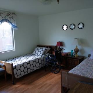 A cozy bedroom with two single beds and a wheelchair, featuring wall decorations and a lamp.