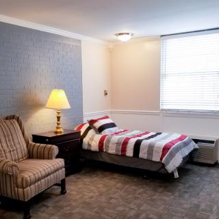 A cozy bedroom with a single bed, lamp, and armchair by the window.