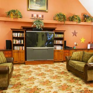 A vintage-style living room with a large television, wooden shelves, floral carpet, and comfortable sofas.