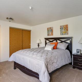 A cozy bedroom with a neatly made bed, nightstand, lamps, and a closet with sliding doors.