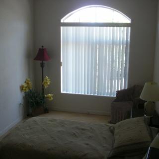 A minimalist bedroom with a bed, lamp, and window blinds.