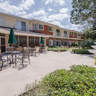 A sunny outdoor patio area with tables, chairs, and umbrellas in front of a residential building.
