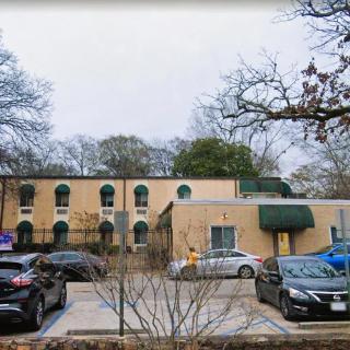 An urban building with a parking lot in front, surrounded by trees.