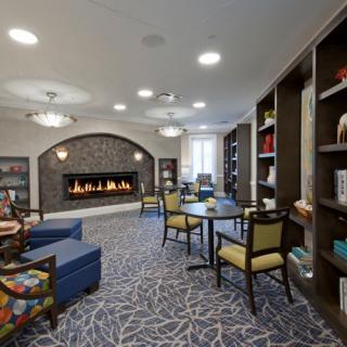 A cozy library interior featuring a fireplace, comfortable seating, and bookshelves.