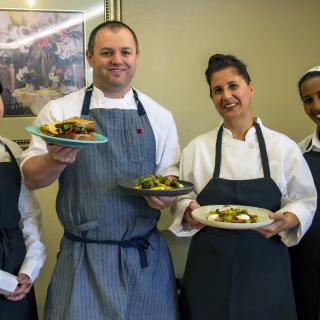 A group of chefs proudly presenting their dishes in a kitchen setting.