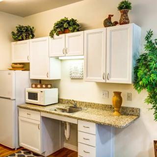 A modern kitchen with white cabinets and granite countertops, featuring a microwave, sink, and refrigerator.