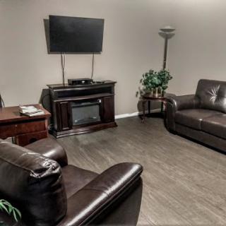 A cozy living room setup featuring dark leather sofas, a TV mounted on the wall, and a warm ambiance.