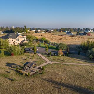 A serene aerial view of a landscaped garden with a pathway and a house in the background, set in a peaceful countryside.