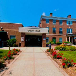 The entrance to a residential building, surrounded by vibrant flowers and under a clear blue sky.