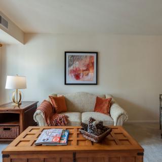 A cozy living room featuring a sofa with decorative pillows, a wooden coffee table with magazines and decor, and a lamp beside it.