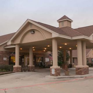 A building with a covered entrance and driveway, featuring pillars and a peaked roof.