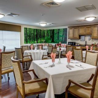 A well-decorated dining room with neatly arranged tables and chairs, featuring elegant table settings and warm lighting.