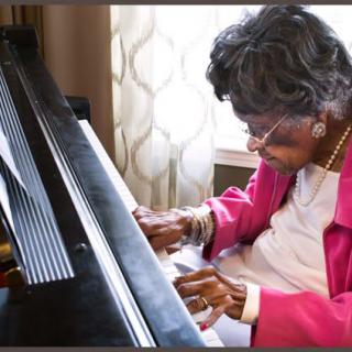 An elderly woman playing the piano with focus and passion indoors.