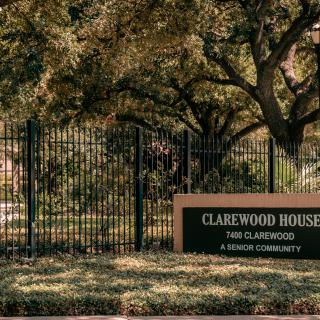 Entrance sign for Clarewood House, a senior community, surrounded by trees and a fence.